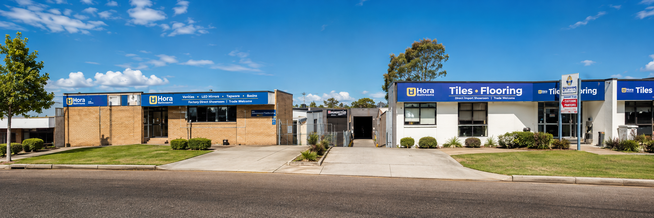 A wide exterior view of a commercial building complex with multiple brick and white storefronts under a blue sky.